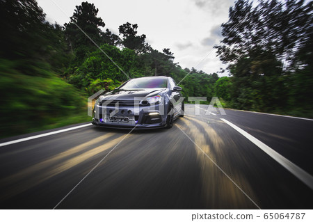 Blue sedan driving across natural rain forests under the sunlight Blue sedan driving across natural rain forests under the sunlight 65064787