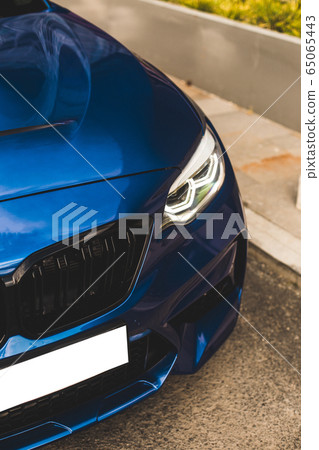 Blue sport sedan parked in the street ,front lights and bumper view 65065443