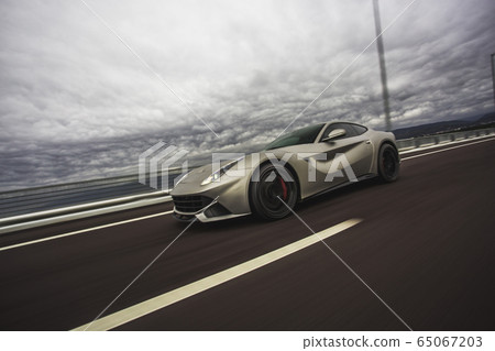 Silver sport racing car autoshow in a stormy weather under clouds on the highway 65067203