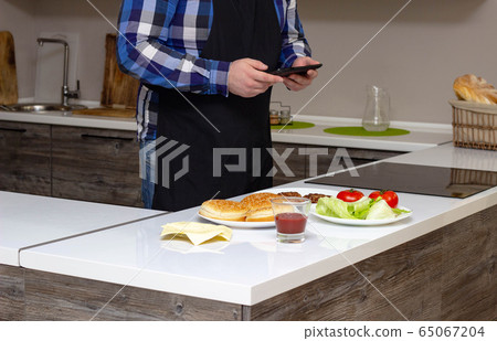 Man photographs cooking home burger on the phone, background 65067204