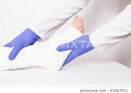 The doctor conducts a medical examination of the patient with a dislocation on the ankle joint of the leg. Bandage overlay concept, white background, medical The doctor conducts a medical examination of the patient with a dislocation on the ankle joint of the leg. Bandage overlay concept, white background, medical 65067631