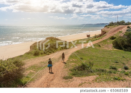 Two girls athletes in sports uniforms, walk along the cliff shore, in the summer near the sea. Beach of Falesia, Vilamoura Albufeira, Portugal. 65068589