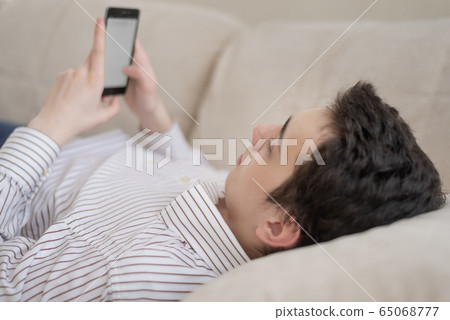 Teenager young man lying on sofa at home, holding 65068777
