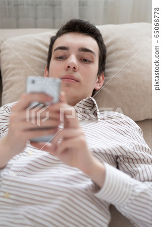 Teenager young man lying on sofa at home, holding Teenager young man lying on sofa at home, holding 65068778