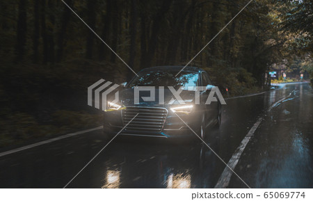 Driving blue car, yellow lights on in the dark forest in shower rain on the moist asphalt,front view Driving blue car, yellow lights on in the dark forest in shower rain on the moist asphalt,front view 65069774
