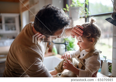 Father checking forehead of sick toddler daughter indoors at home. Father checking forehead of sick toddler daughter indoors at home. 65070985
