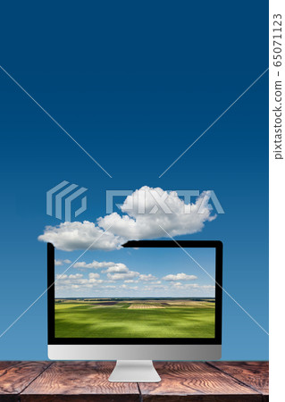 Monitor with landscape on a wooden table and blue sky background. 65071123