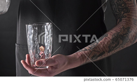 A man with a tattoo is pouring ice cubes into a glass around a dark background. 4K UHD video, 2160p. A man with a tattoo is pouring ice cubes into a glass around a dark background. 4K UHD video, 2160p. 65071376