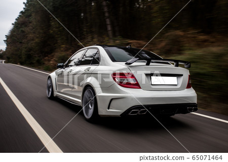White sedan with red lights on the forest road in the evening, view from behind White sedan with red lights on the forest road in the evening, view from behind 65071464