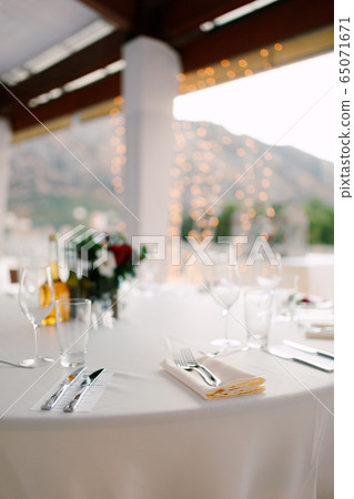 Close-up of a wedding dinner table - forks lie on a napkin. Table in background of the garland, on the table are glasses for wine and glasses, floral composition and carafe with olive oil Close-up of a wedding dinner table - forks lie on a napkin. Table in background of the garland, on the table are glasses for wine and glasses, floral composition and carafe with olive oil 65071671