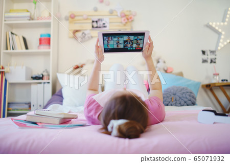 Young girl with tablet on bed, relaxing during quarantine. Copy space. 65071932