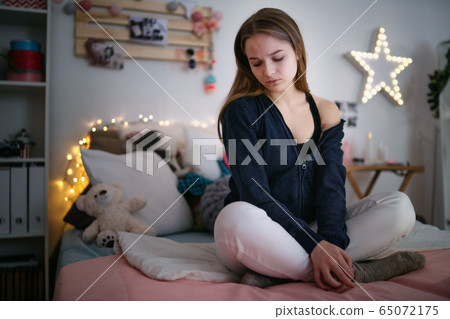 Worried young girl sitting indoors on bed, online dating concept. 65072175