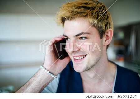 Close-up of young man with smartphone indoors at home, making phone call. 65072214