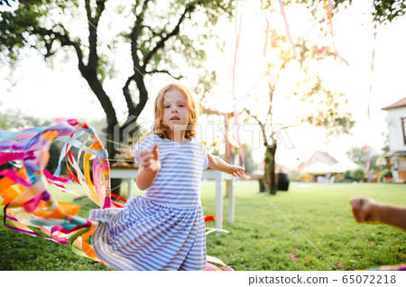Small girl outdoors in garden in summer, playing with rainbow hand kite. Small girl outdoors in garden in summer, playing with rainbow hand kite. 65072218