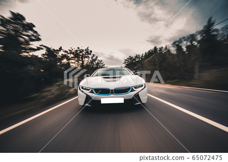 White sport car high speed drive in the forest across green trees, front view 65072475