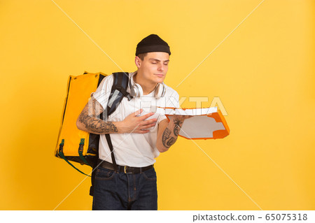 Contacless delivery service during quarantine. Man delivers food and shopping bags during insulation. Emotions of deliveryman isolated on yellow background. Contacless delivery service during quarantine. Man delivers food and shopping bags during insulation. Emotions of deliveryman isolated on yellow background. 65075318