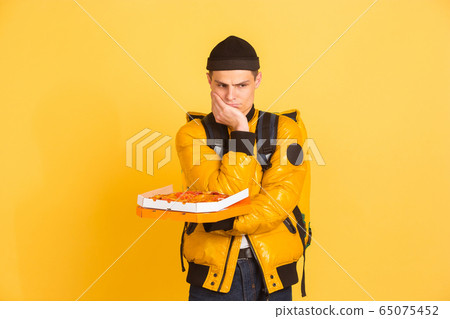 Contacless delivery service during quarantine. Man delivers food and shopping bags during insulation. Emotions of deliveryman isolated on yellow background. 65075452
