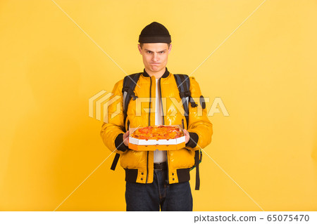 Contacless delivery service during quarantine. Man delivers food and shopping bags during insulation. Emotions of deliveryman isolated on yellow background. 65075470