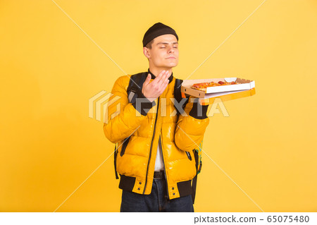 Contacless delivery service during quarantine. Man delivers food and shopping bags during insulation. Emotions of deliveryman isolated on yellow background. 65075480