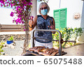 elderly lady cooking on a barbecue with face mask 65075488