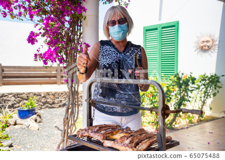 elderly lady cooking on a barbecue with face mask elderly lady cooking on a barbecue with face mask 65075488