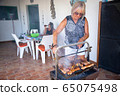 happy elderly lady cooking on a barbecue together with her family 65075498