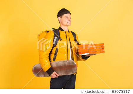 Contacless delivery service during quarantine. Man delivers food and shopping bags during insulation. Emotions of deliveryman isolated on yellow background. Contacless delivery service during quarantine. Man delivers food and shopping bags during insulation. Emotions of deliveryman isolated on yellow background. 65075517