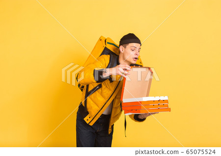 Contacless delivery service during quarantine. Man delivers food and shopping bags during insulation. Emotions of deliveryman isolated on yellow background. Contacless delivery service during quarantine. Man delivers food and shopping bags during insulation. Emotions of deliveryman isolated on yellow background. 65075524
