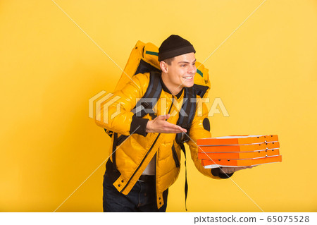 Contacless delivery service during quarantine. Man delivers food and shopping bags during insulation. Emotions of deliveryman isolated on yellow background. Contacless delivery service during quarantine. Man delivers food and shopping bags during insulation. Emotions of deliveryman isolated on yellow background. 65075528