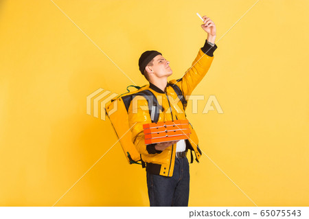Contacless delivery service during quarantine. Man delivers food and shopping bags during insulation. Emotions of deliveryman isolated on yellow background. Contacless delivery service during quarantine. Man delivers food and shopping bags during insulation. Emotions of deliveryman isolated on yellow background. 65075543