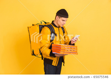 Contacless delivery service during quarantine. Man delivers food and shopping bags during insulation. Emotions of deliveryman isolated on yellow background. Contacless delivery service during quarantine. Man delivers food and shopping bags during insulation. Emotions of deliveryman isolated on yellow background. 65075546