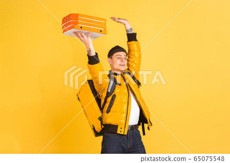 Contacless delivery service during quarantine. Man delivers food and shopping bags during insulation. Emotions of deliveryman isolated on yellow background. Contacless delivery service during quarantine. Man delivers food and shopping bags during insulation. Emotions of deliveryman isolated on yellow background. 65075548