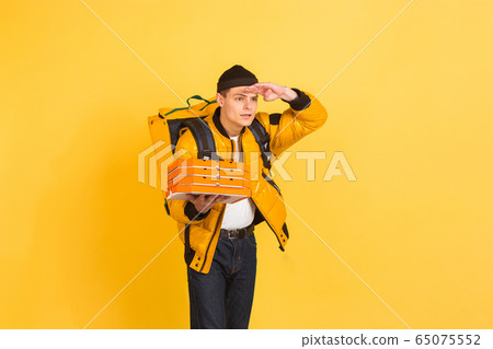 Contacless delivery service during quarantine. Man delivers food and shopping bags during insulation. Emotions of deliveryman isolated on yellow background. Contacless delivery service during quarantine. Man delivers food and shopping bags during insulation. Emotions of deliveryman isolated on yellow background. 65075552