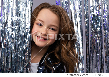 European beautiful teenage girl in a stylish outfit on a holiday peeks out from behind a tinsel 65078685