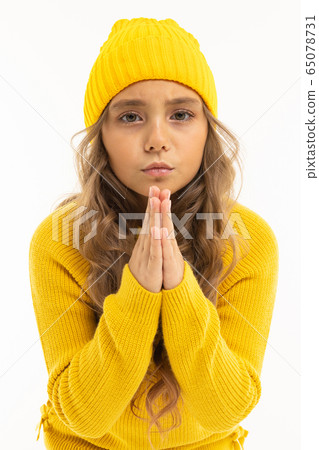 European attractive girl in a yellow hat and jacket folded her hands in front of herself on a white 65078731