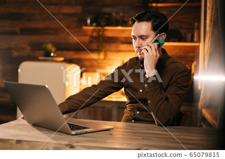 Businessman working on laptop and talking on mobile phone at the home Businessman working on laptop and talking on mobile phone at the home 65079815