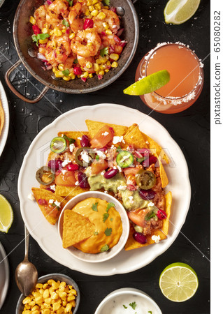 Mexican food, a flat lay on a black background. Nachos, shrimps, Paloma cocktails, shot from the top Mexican food, a flat lay on a black background. Nachos, shrimps, Paloma cocktails, shot from the top 65080282