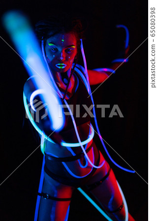 Portrait of a Girl with Glowing Tubes in Neon UF Light. Model Girl with Dreadlocks and Fluorescent Creative Psychedelic MakeUp, Art Design of Female Disco Dancer Model in UV, Colorful Abstract Make-Up Portrait of a Girl with Glowing Tubes in Neon UF Light. Model Girl with Dreadlocks and Fluorescent Creative Psychedelic MakeUp, Art Design of Female Disco Dancer Model in UV, Colorful Abstract Make-Up 65080398