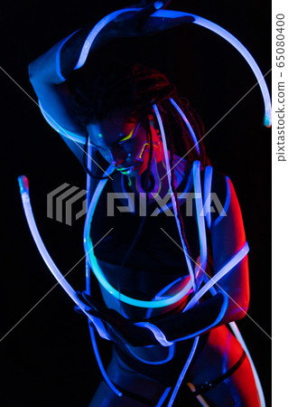 Portrait of a Girl with Glowing Tubes in Neon UF Light. Model Girl with Dreadlocks and Fluorescent Creative Psychedelic MakeUp, Art Design of Female Disco Dancer Model in UV, Colorful Abstract Make-Up Portrait of a Girl with Glowing Tubes in Neon UF Light. Model Girl with Dreadlocks and Fluorescent Creative Psychedelic MakeUp, Art Design of Female Disco Dancer Model in UV, Colorful Abstract Make-Up 65080400