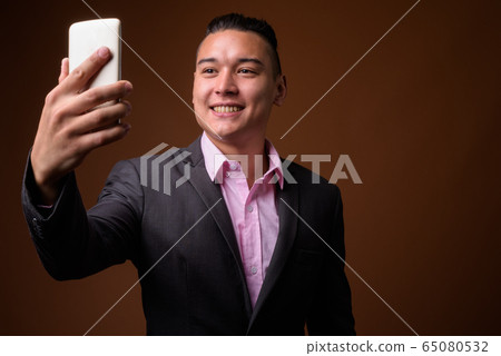 Young handsome multi-ethnic businessman against brown background Young handsome multi-ethnic businessman against brown background 65080532