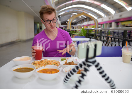 Young man vlogging with mobile phone in Indian restaurant Young man vlogging with mobile phone in Indian restaurant 65080693