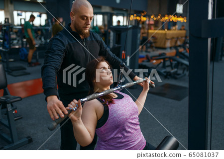 Instructor helps to overweight woman, gym Instructor helps to overweight woman, gym 65081037