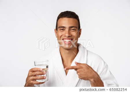 An attractive man drinking a glass of water against white background 65082254