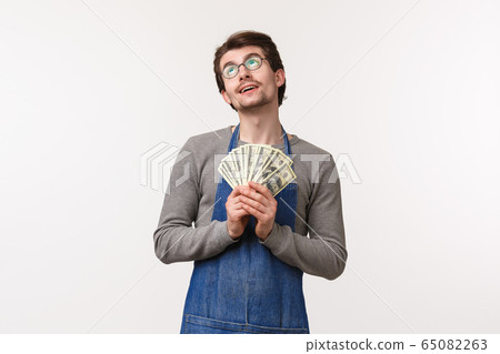 Small business, finance and career concept. Portrait of dreamy delighted handsome man in apron, employee receive his paycheck, holding earned money and dreaming of vacation, white background Small business, finance and career concept. Portrait of dreamy delighted handsome man in apron, employee receive his paycheck, holding earned money and dreaming of vacation, white background 65082263