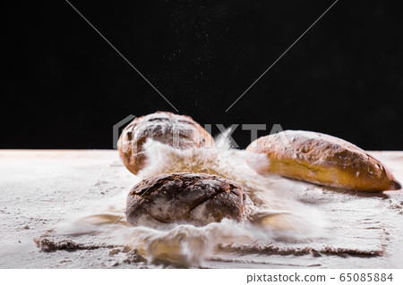 Traditional artisan rye bread loaf fall into flour. Dark background. Bakery and homemade rustic bread concept. 65085884