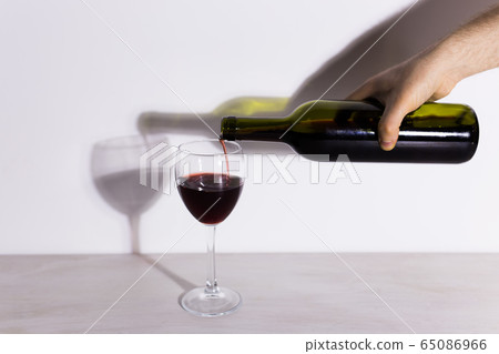 Pouring red wine into the glass against wooden background Pouring red wine into the glass against wooden background 65086966