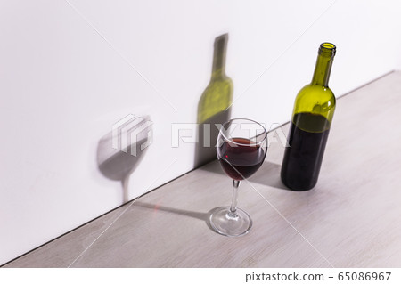 A glass of wine and a bottle casts a long shadow from the evening sun. 65086967