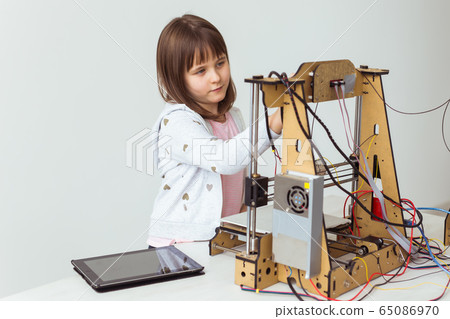 Cute girl with 3d printed shutter shades is watching her 3d printer as it prints her 3d model. 65086970