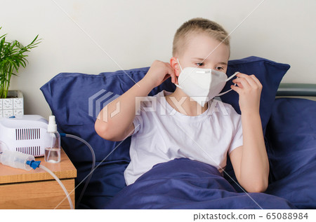 Sick boy putting on medical protective mask. Child sits on bed. Sick boy putting on medical protective mask. Child sits on bed. 65088984
