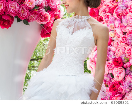Beautiful bride in a wedding dress posing on a decorative background of pink flowers Beautiful bride in a wedding dress posing on a decorative background of pink flowers 65089801